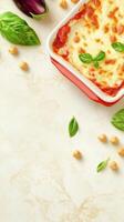Delicious lasagna in a red dish with basil and eggplant on light marble background. Copy space for text photo