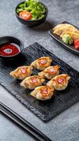 Dumplings on slate plate served with sauce and salad on gray table background for menu design photo
