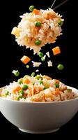 Fried rice with chopsticks and vegetables is lifted from bowl with dark background for food blog use photo