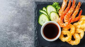 Fried shrimp and onion rings served with cucumber and sauce on a slate board for dinner use photo