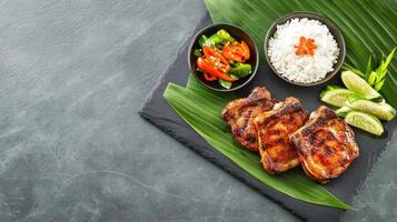 Grilled chicken with rice, vegetables, and limes on a leaf, set against a stone background photo