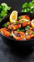 Grilled fish cubes in black bowl with lemon and parsley, on table. Food blog or restaurant use photo
