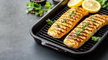 Grilled salmon fillets with lemon on a pan, herbs in background. Use food blog photo