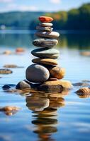 Tranquil stone stack by calm lake. A stack of smooth stones balances on a rock in clear water, reflecting serenity and harmony in nature. photo