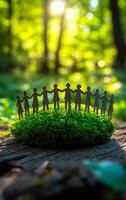 Figures unite in green woods. Small metallic figures stand hand in hand atop lush green moss in a vibrant forest, symbolizing unity and connection. photo