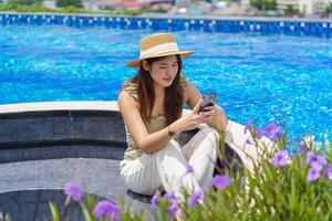 a woman in a hat sitting by a pool using her phone photo