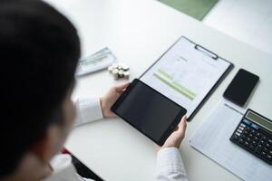 businessman using tablet computer at desk with calculator and papers photo