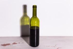 Bottle with wine, red puddle of wine on the table. Cleaning after party concept. photo