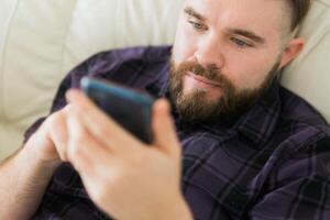 Bored lazy man close up relaxed and use smartphone for killing time alone in apartment - social media and gadget addiction concept photo