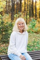 Senior woman relaxing on a bench in an autumn park. Concept of aging gracefully, wellbeing, emotional calmness, leisure and joy of simple outdoor pleasures photo