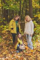 Portrait of three generations of happy beautiful women and dog looking at camera, hugging and smiling in autumn nature. photo
