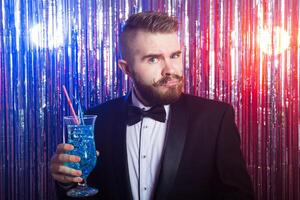 Club party, emotions and holidays concept - Portrait of elegant angry handsome man in a expensive suit holds blue cocktail on shiny background. photo