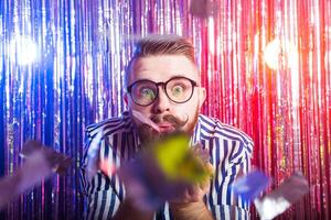 Party, carnival, holidays and fun concept - Fancy male blowing confetti against shiny background. photo