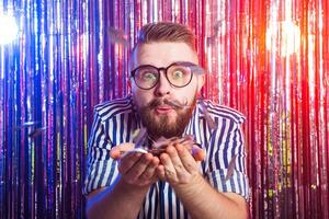 Party, carnival, holidays and fun concept - Fancy man blowing confetti against shiny background photo