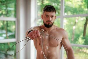 Holding jump rope. Strong muscular man is working out in the gym photo