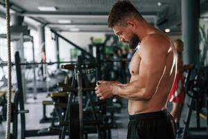 With smartphone,, taking a break. Strong muscular man is working out in the gym photo