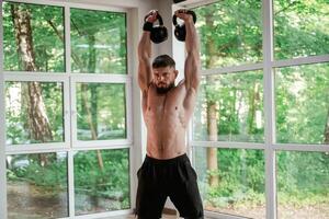 Against ,the ,,windows. With dumbbells. Strong muscular man is working out in the gym photo