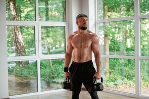 Standing,, holding dumbbells. ..Strong muscular man is working out in the gym photo