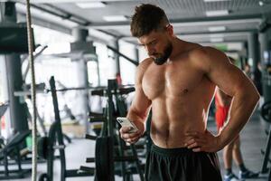 With ,smartphone, taking a break. Strong muscular man is working out in the gym photo