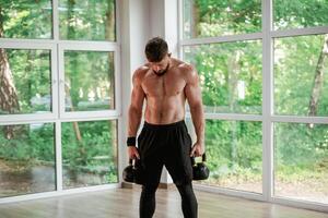 Standing, holding ,dumbbells. Strong muscular man is working out in the gym photo