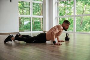 Green trees outside the windows. Strong muscular man is working out in the gym photo