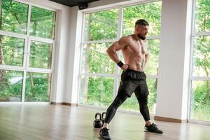 Daytime, trees, ,outside the windows. Strong muscular man is working out in the gym photo