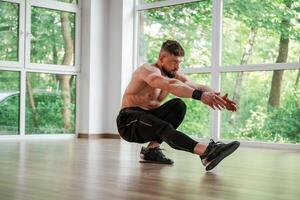 Daytime, trees ,outside the windows.. Strong muscular man is working out in the gym photo