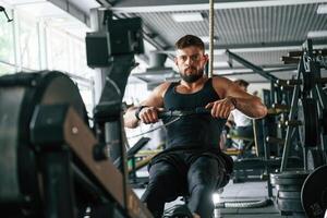 Sitting, doing stamina exercise. Strong muscular man is working out in the gym photo