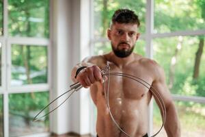 Holding, jump rope. Strong muscular man is working out in the gym photo