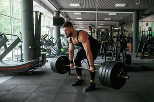 Big, and heavy barbell in hands. Strong muscular man is working out in the gym photo