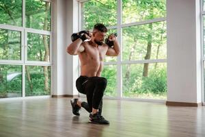 With heavy, dumbbells. Strong muscular man is working out in the gym photo