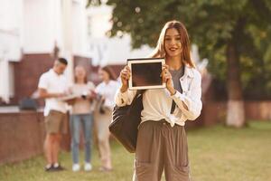 Woman is showing digital tablet, copy space. Group of students are outside together photo