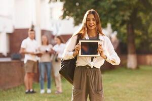 Woman, is showing digital tablet,,, copy space. Group of students are outside together photo