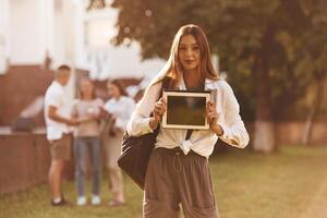 Woman is showing digital tablet, copy space. Group of students are outside t,,ogether photo