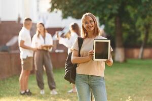 Girl is with, digital tablet. Group of students are outside together photo