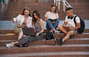 Relaxed,, on the stairs, with laptop. Group of students are outside together photo