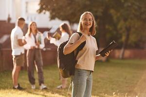 Girl is ,with digital tablet. Group of students are outside together photo