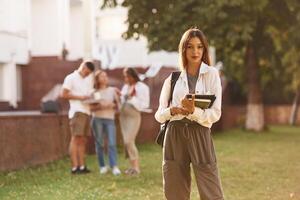 Beautiful, woman is standing in front of her friends. Group of students are outside photo