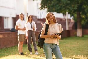 Girl is ,,with digital tablet. Group of students are outside together photo