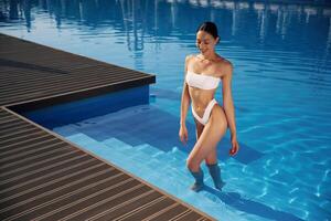 Going ,up out the ,water. Beautiful woman in bikini is resting by the pool photo