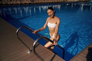 Going ,up, out the water. Beautiful woman in bikini is resting by the pool photo