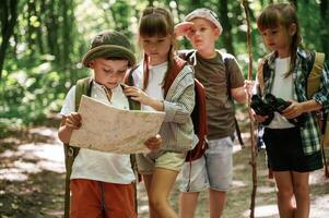 Smart ,boy is, reading the map. Kids in forest at summer daytime together photo