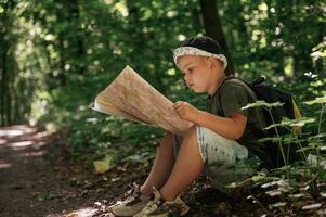 Little kid, tourist is sitting and reading the map in the forest photo