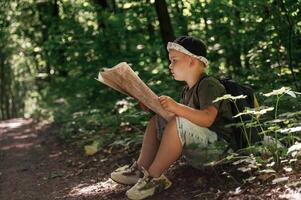 Little, kid tourist is sitting and reading the map in the forest photo