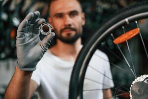 Holding circle shaped part near the wheel. Repair man in bicycle shop, working in store photo