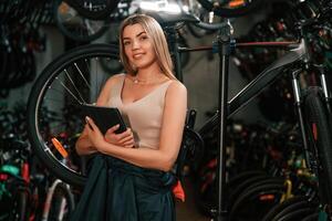 Information in the digital tablet, standing. Repair woman in bicycle shop, working in store photo