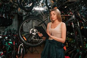 Information, in the digital tablet, standing. Repair woman in bicycle shop, working in store photo