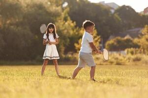 Rackets in hands, playing badminton. Happy kids are on the summer field photo