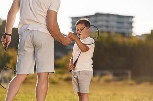 With badminton rackets. Father and little son are together on the summer field, photo