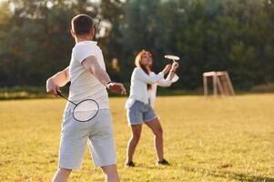 Weekend, activities. Man with woman are playing badminton on the field photo